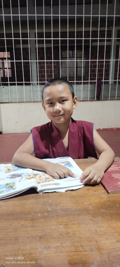 Niño en un monasterio leyendo un libro sobre una mesa de madera.