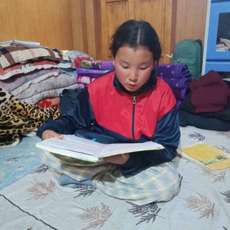 Niña leyendo un libro sentada en el suelo, rodeada de mantas.