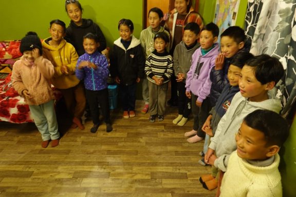 Grupo de niños y adultos reunidos en una habitación con paredes verdes.