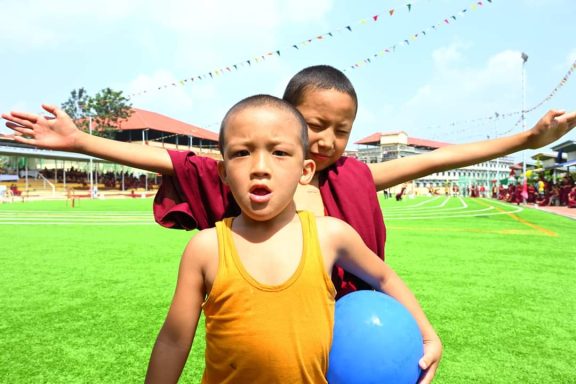 Niños monjes budistas jugando en un campo verde, uno sosteniendo una pelota azul.