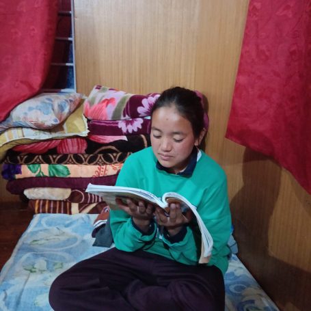 Niña sentada en el suelo, leyendo un libro rodeada de cojines y mantas.