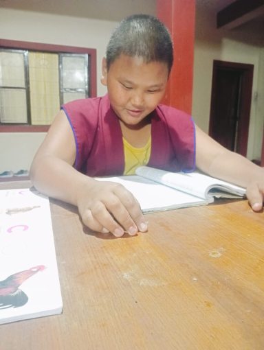 Niño sentado en una mesa, leyendo un libro con concentración.