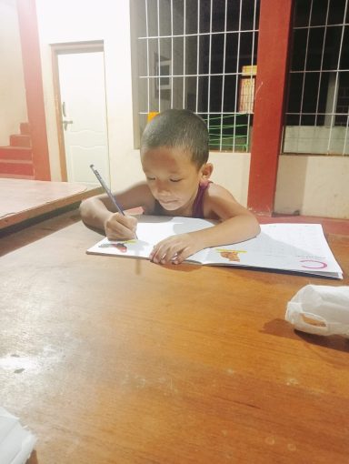 Niño sentado en una mesa, dibujando y concentrado en su tarea.