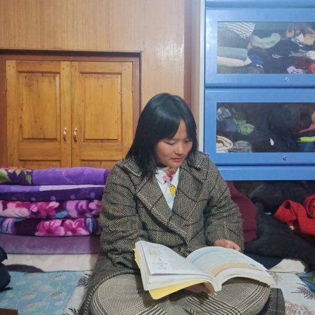 Niña sentada en el suelo, leyendo un libro en un entorno hogareño.