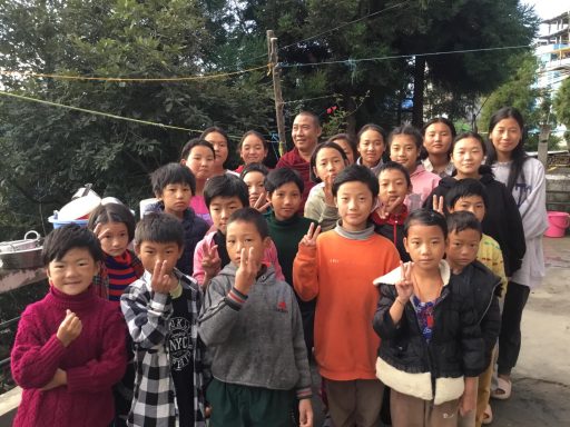 Grupo de niños y adultos posando al aire libre, sonriendo y haciendo señales con las manos.